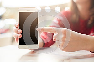 Selective focus. Unrecognizable female keeps modern white smart phone in hand, points with finger at blank copy screen for your te