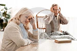 selective focus of upset retired woman sitting near husband with mental illness.