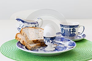 Selective focus view of boiled egg in pretty painted ceramic holder and slices of bread in plate