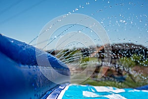 Selective focus on water spray shooting across a slip and slide perched on the top of a hill