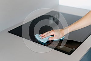 Selective focus on woman hand holding blue rug and cleaning black empty ceramic stove