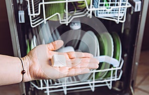 Selective focus on woman hand, holding homemade natural dishwasher pod defocus dishes in dishwasher on background. photo