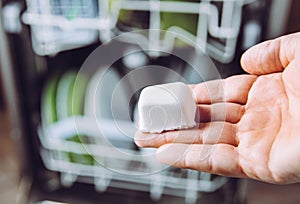 Selective focus on woman hand, holding homemade natural dishwasher pod defocus dishes in dishwasher on background.