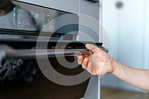 Selective focus on woman hand opening glass door of electric oven in modern kitchen