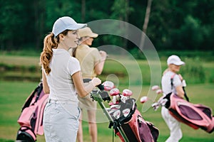 selective focus of women in caps with golf gear walking on green lawn