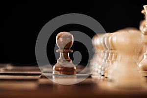 Selective focus of wooden chessboard with chess pieces and pawn in front isolated on black .