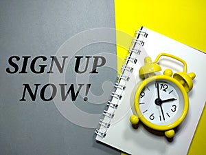 Selective focus.Word SIGN UP NOW with clock on a notebook with gray and yellow background.