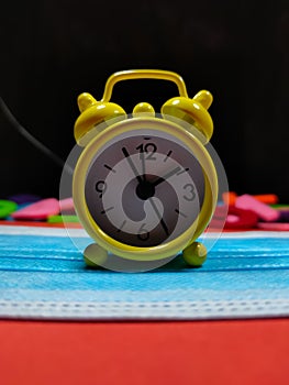 Selective focus.A yellow clock on face mask with blur bsckground.Time and pendemic concept idea.Shot were noise and film grain.