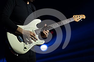 Selective focus on young Asian man guitarist`s hand playing electric guitar solo with full spectrum of light at concert