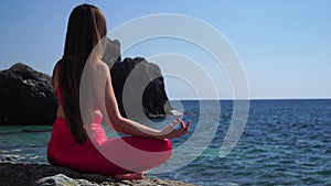 Selective focus. Young beautiful caucasian woman in a red suit practicing yoga on the beach at sunrise near the sea