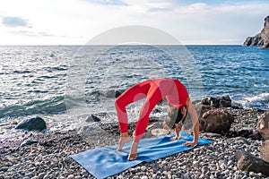 Selective focus. Young beautiful caucasian woman in a red suit practicing yoga, fitness and scretching on the beach at sunrise