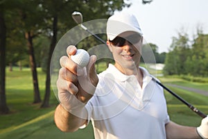 Selective focus of a young male golfer holding golf ball out in