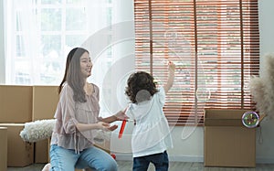 Selective focus on young mother at home looking at her little cute girl having fun playing soap bubbles, catching and chasing soap