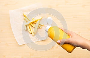 Selective focus of youngwoman squeezing a bottle sauce  mustard  for dipping with french fried on wood table background