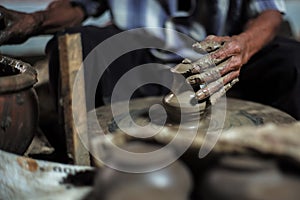 Selective focused on the dirty wrinkled skin hands of old man molding the clay work on the spinning wheel for making the jar with