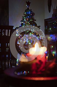 Selective shot of a burning candle and beautiful Christmas tree with colorful lights