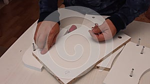 Self-assembly of furniture. A man installs cams in the wooden elements of a tabletop shelf