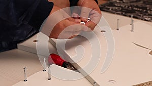 Self-assembly of furniture. A man installs cams in the wooden elements of a tabletop shelf. Close-up