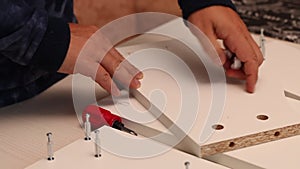 Self-assembly of furniture. A man installs cams in the wooden elements of a tabletop shelf. Close-up