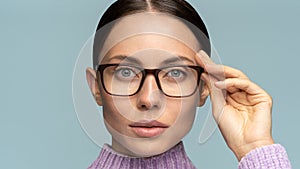 Self-assured confident business woman touches eyeglasses, looking at camera,  on studio blue background