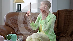 Self-assured grey-haired slim woman examining face and neck looking in hand mirror smiling. Positive Caucasian middle