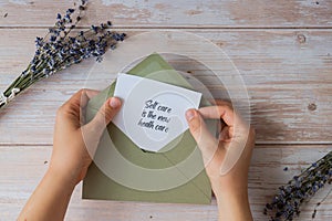 SELF CARE IS THE NEW HEALTH CARE text on supportive message paper note reminder from green envelope. Flat lay