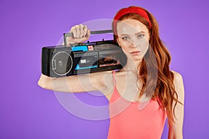Self-confident girl looks with focused attention in camera, holds portable audio player