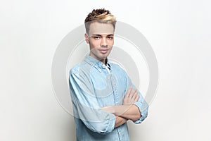 Self-confident handsome man wearing denim shirt standing with crossed arms, looking at camera,