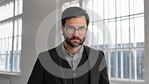 Self-confident and successful man with beard and eyeglasses looking at camera, portrait in building