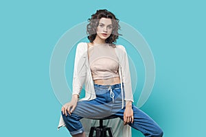 Self-confident woman sitting on chair like fashion model and looking at camera with serious face.