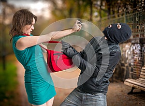 Self defense concept. Young woman was attacked by man in balaclava is using pepper spray photo