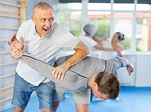 Self defense lesson - elderly man twists the arm of attacking man with painful hold in gym