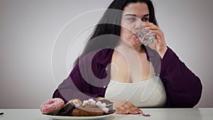 Self-disciplined plump Caucasian woman taking metabolism pill, moving plate with pastry away and smiling. Obese girl