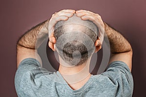 Self-doubt and inferiority complex. Baldy adult man grabs his head with his hands. Rear view. Brown background. The