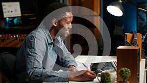 Self employed Black man multitasking at home taking handwritten notes