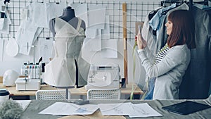 Self-employed female tailor is checking clothing patterns pinned to tailoring dummy then taking photos of it with smart