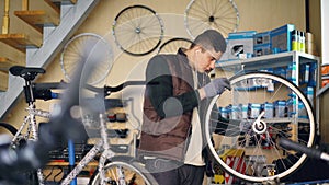Self-employed mechanic is repairing bicycle wheel with wrenches professional instruments while working in small workshop