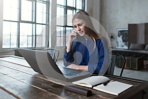 Self-employed woman having a phone conversation while using a computer at home
