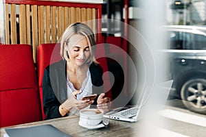 A self-employed woman is working with her phone and laptop on the terrace of a restaurant