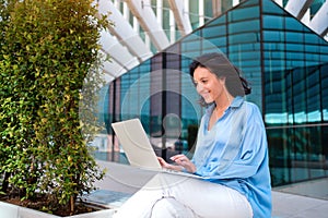 Self employed woman working with laptop sitting outdoor near corporative office building. Pretty business woman freelancer do