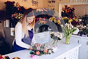 Self-employed young woman owner of florist shop arranging bouquet of roses