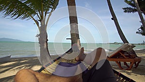 Self enjoying person, face view, lays down on hammock, sea and palms view