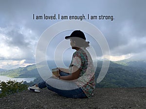 Self healing with affirmation words - I am loved. I am enough. I am strong. With an adventure woman sitting alone holding a cup of photo