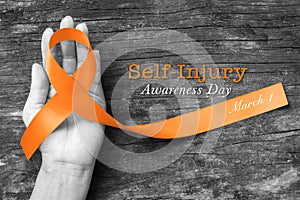 Self- injury awareness day SIAD, March 1with Orange ribbon on human hand old aged background