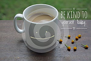 Self Inspirational motivational quote - Be kind to yourself. With smiling mug of white coffee on wooden table and little flowers