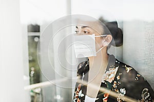 Self isolation coronavirus quarantine. Woman in mask looking outside with hope photo