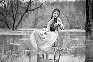 Self-isolation in quarantine. The girl sits on a chair in the water. Pandemic, flood, black and white