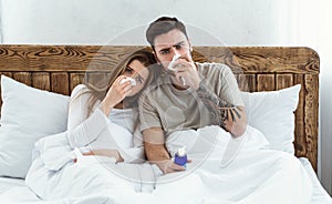 Self-isolation together. Young man and woman in bed wipes nose with napkins