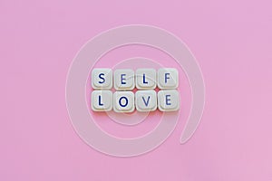 Self love message made with board game letters, over a soft pink background