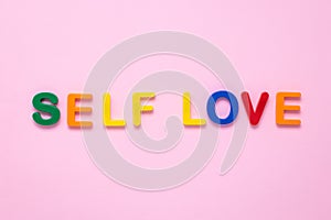 Self love text on pink paper background made from colorful plastic letters. Multicolored inscription on the banner. Title,